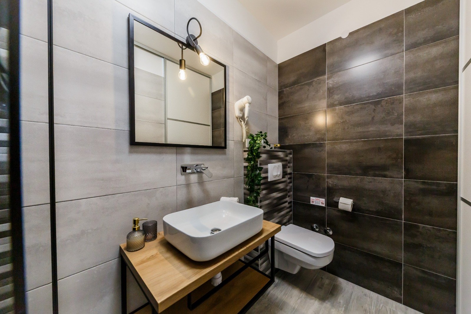 Bathroom with a white vessel basin on a wooden vanity, a black-framed mirror and dark feature tiles.