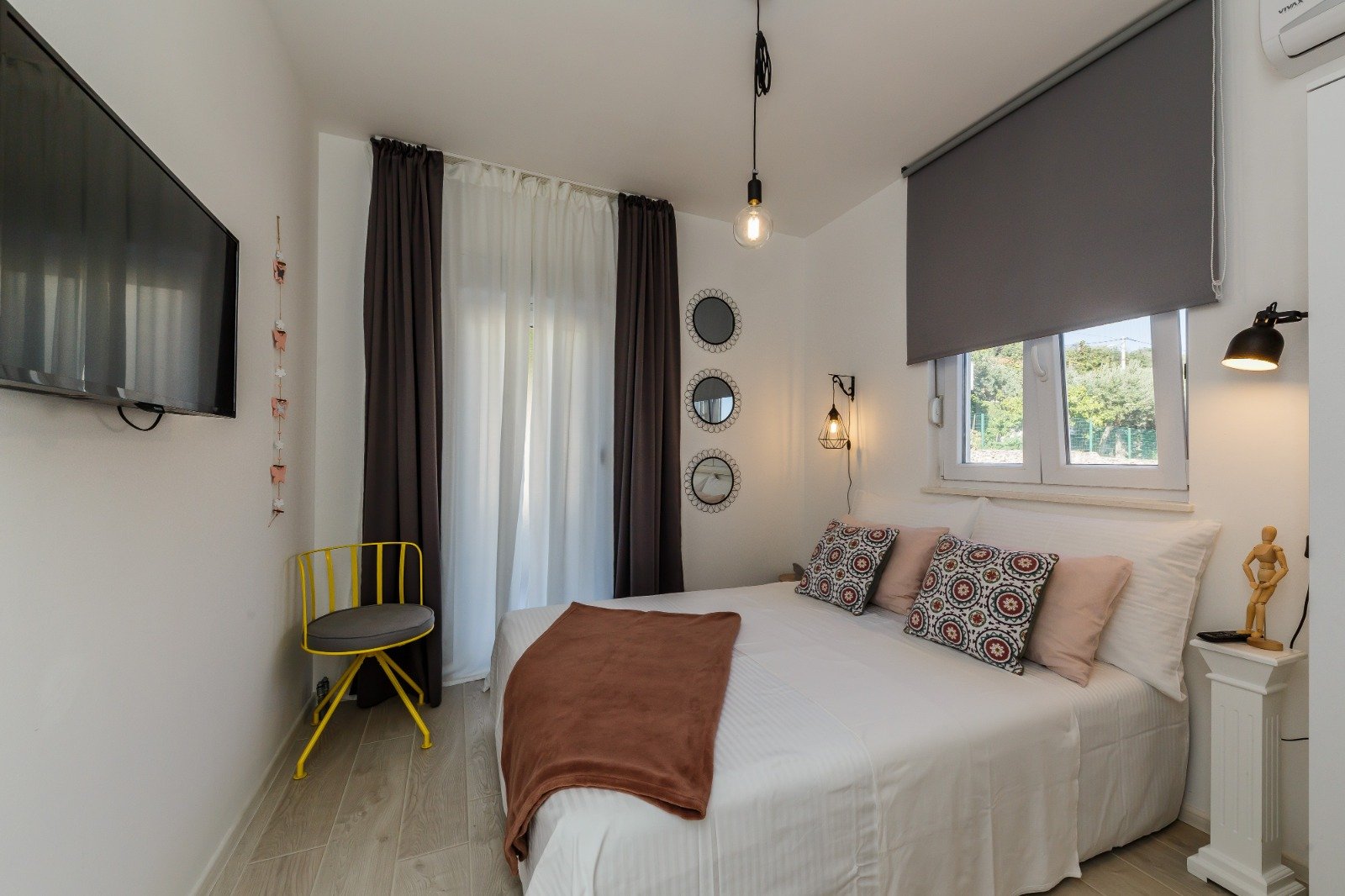 Bedroom with white bedding, patterned cushions, a rust-coloured throw and a yellow accent chair.