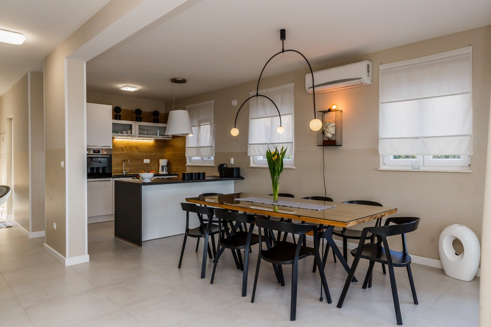 Dining table with black chairs, a vase of tulips and curved pendant lights beside the open kitchen.