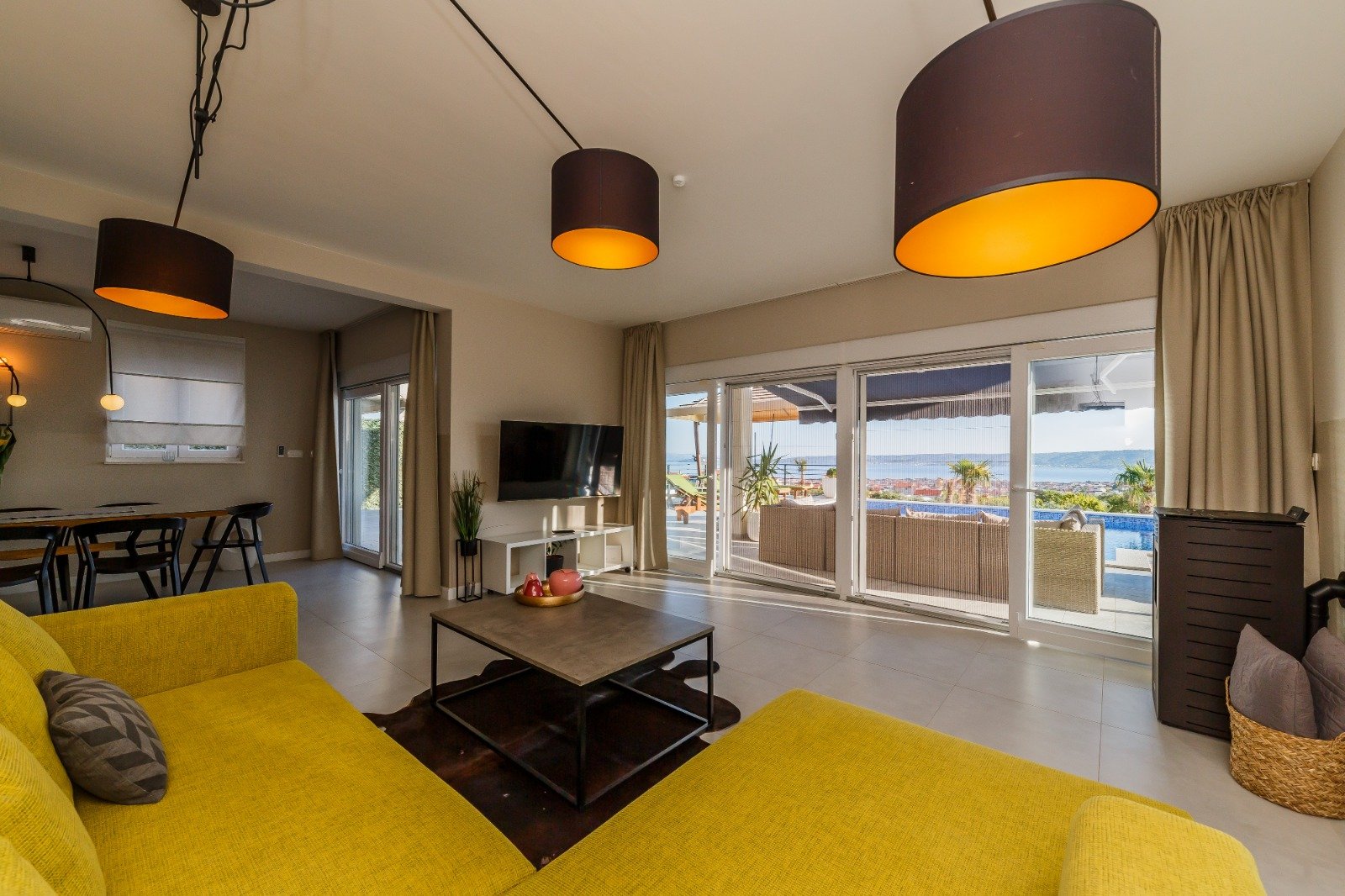 Living room with a yellow sectional sofa and broad glass doors looking across the terrace and pool toward the sea.